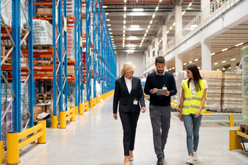 Three people walk through a warehouse, led by a manager reviewing operations.