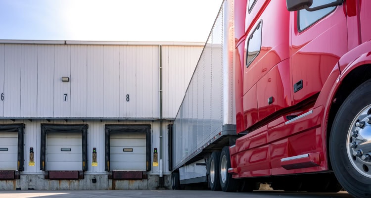 Una foto de un camión con una cabina roja estacionado en el muelle de carga de un almacén.